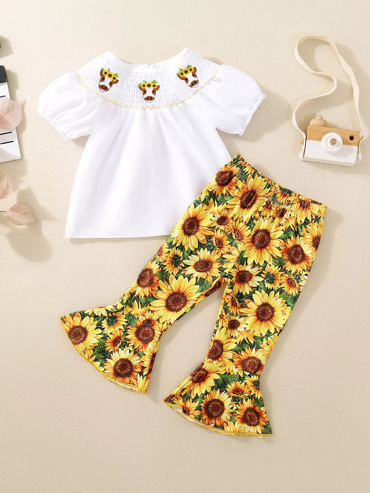 White smocked children’s top with embroidered detail and sunflower-print bell-bottom pants.