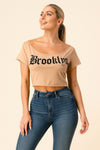 Woman wearing a tan Brooklyn graphic off-shoulder crop top